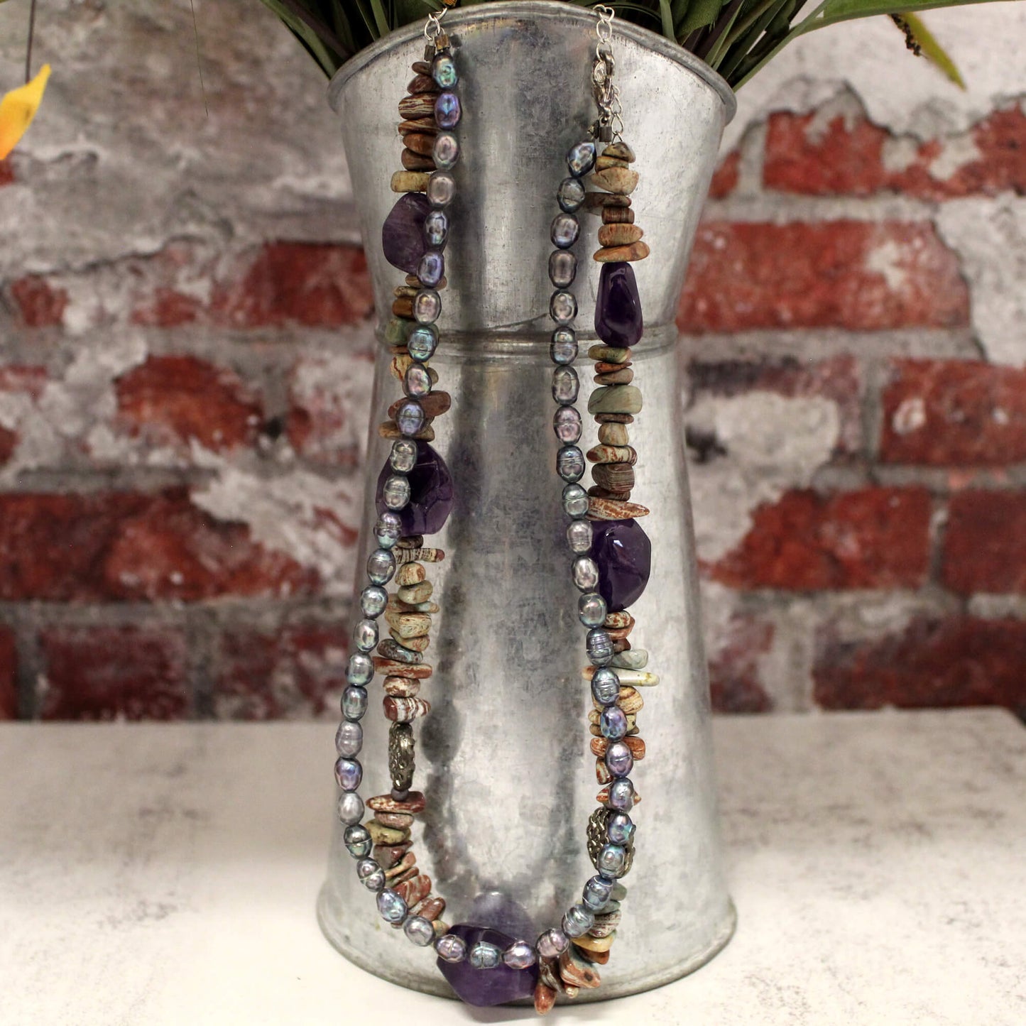 For free-spirited folk and nature lovers, this necklace makes a statement. The raw, organic beauty of the stones paired with the delicate beads evokes a sense of wanderlust. Give your outfit an adventurous twist and connect with the earthy hues of jasper. This eye-catching two-strand design features bold purple stones and chips alongside shiny iridescent beads. Measures 16-18".