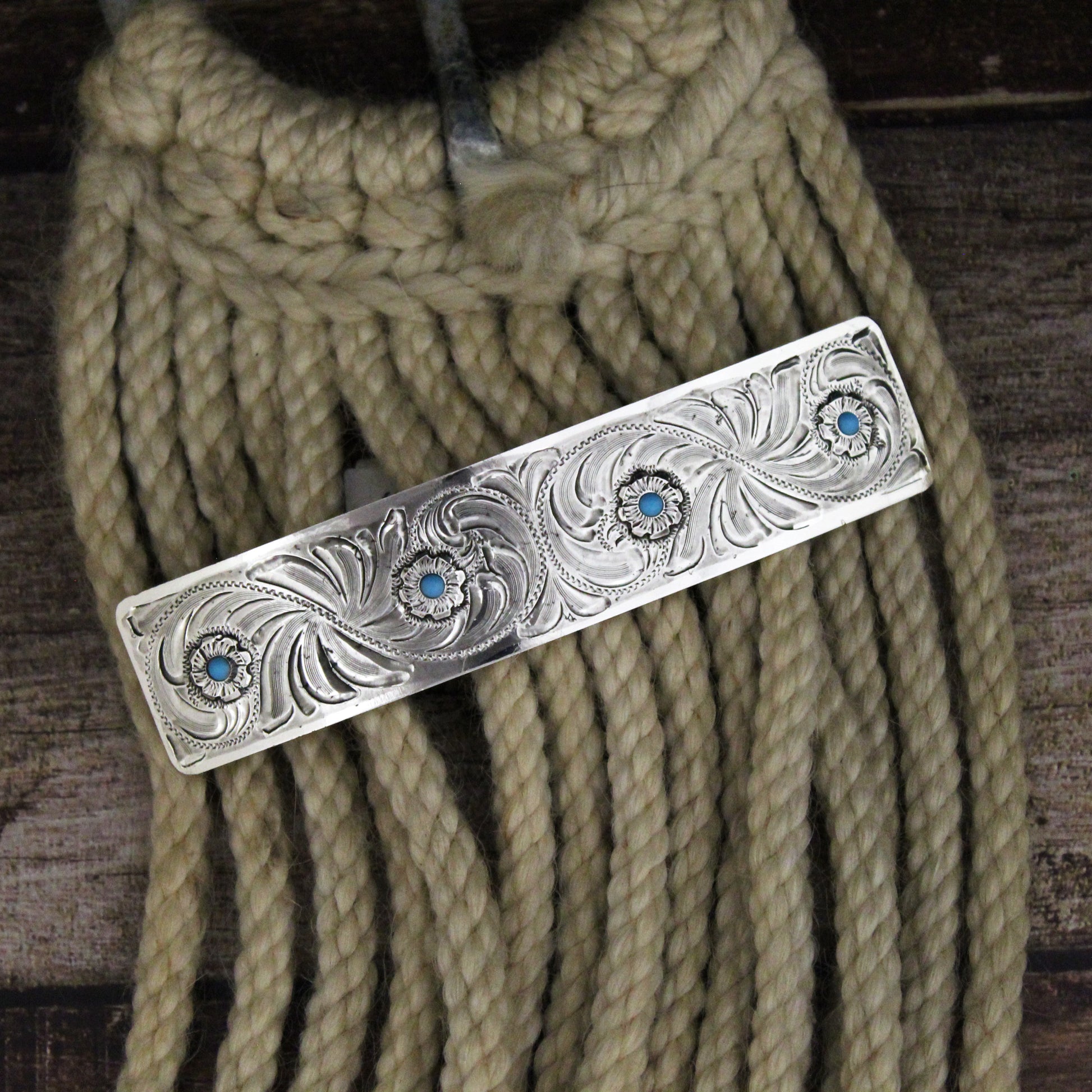 This German silver barrette has been impressed with a leaf and vine design for added texture with four small flowers with a turquoise center. The silver cowgirl barrette is a stylish piece that will add a vintage western feel to your look. Measures 4-1/2" by 1".