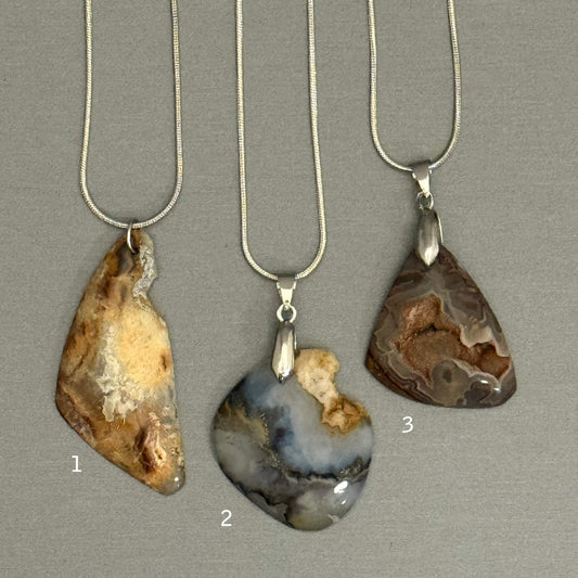 Three agate pendants on silver necklaces against a gray background