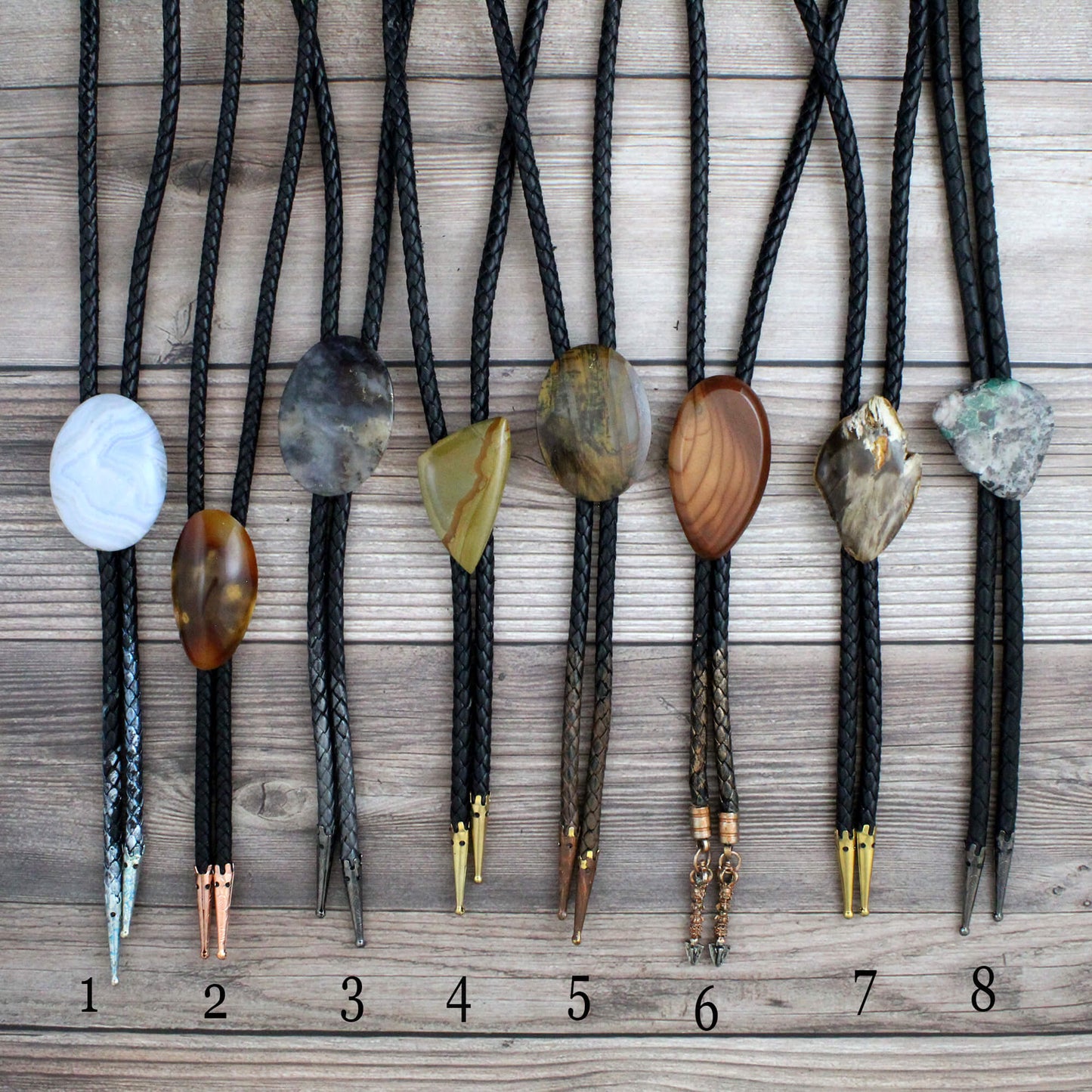Set of eight bolo ties with various stone and metal pendants on a wooden surface.