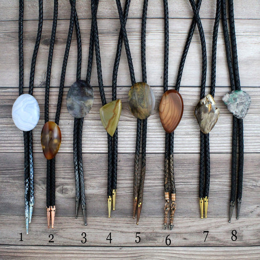 Set of eight bolo ties with various stone and metal pendants on a wooden surface.