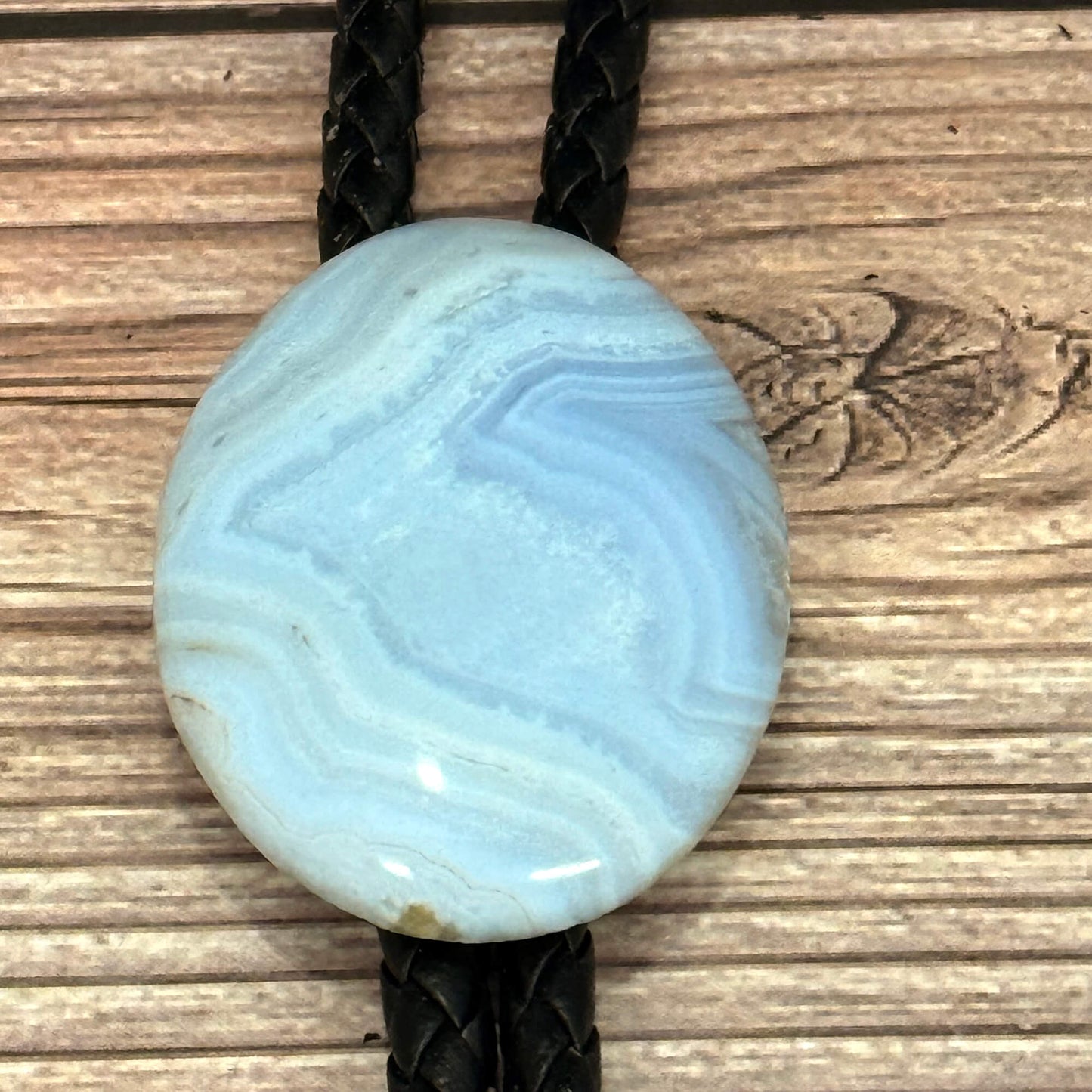 Blue stone pendant on a braided leather cord against a wooden background