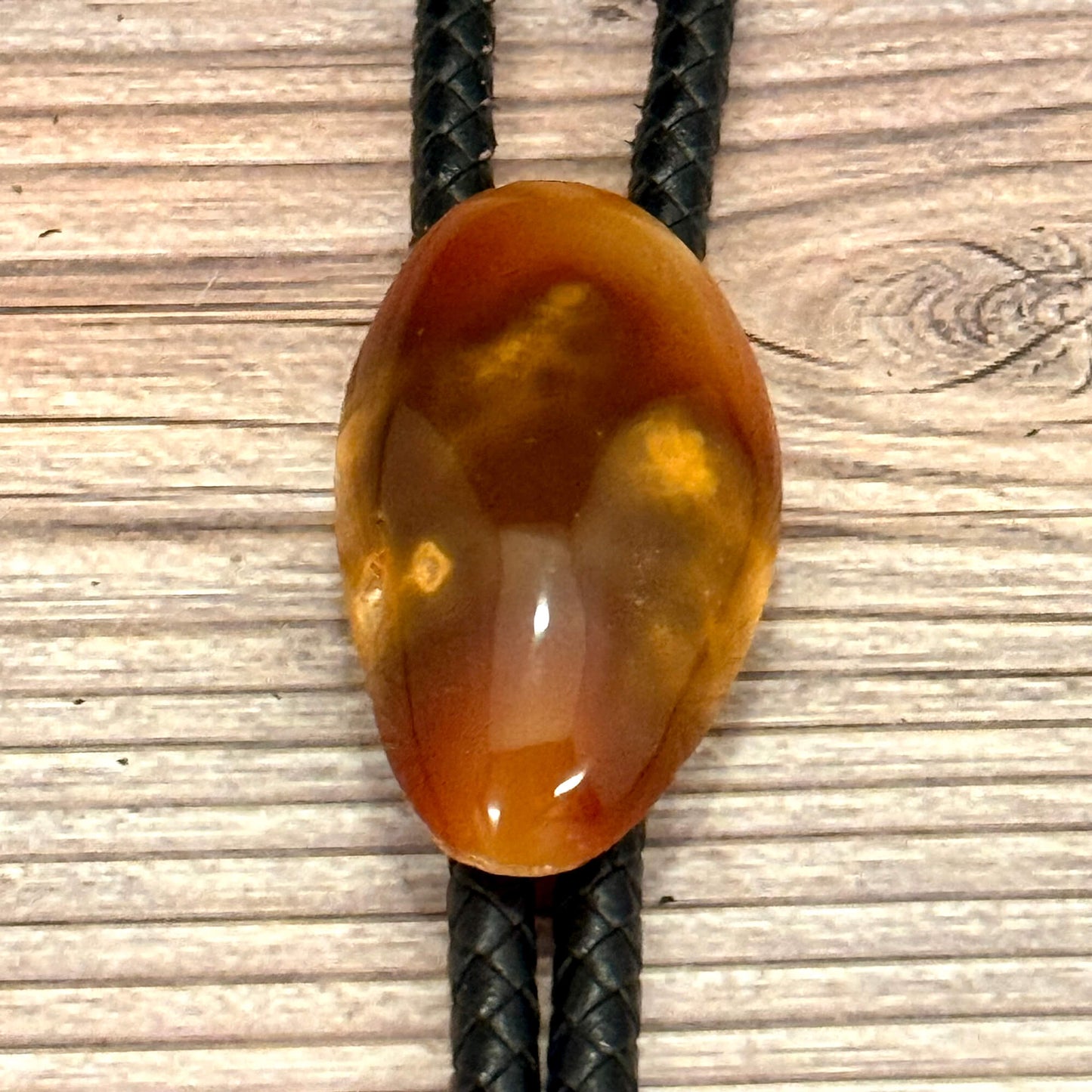 Brown agate stone on a black cord against a wooden background