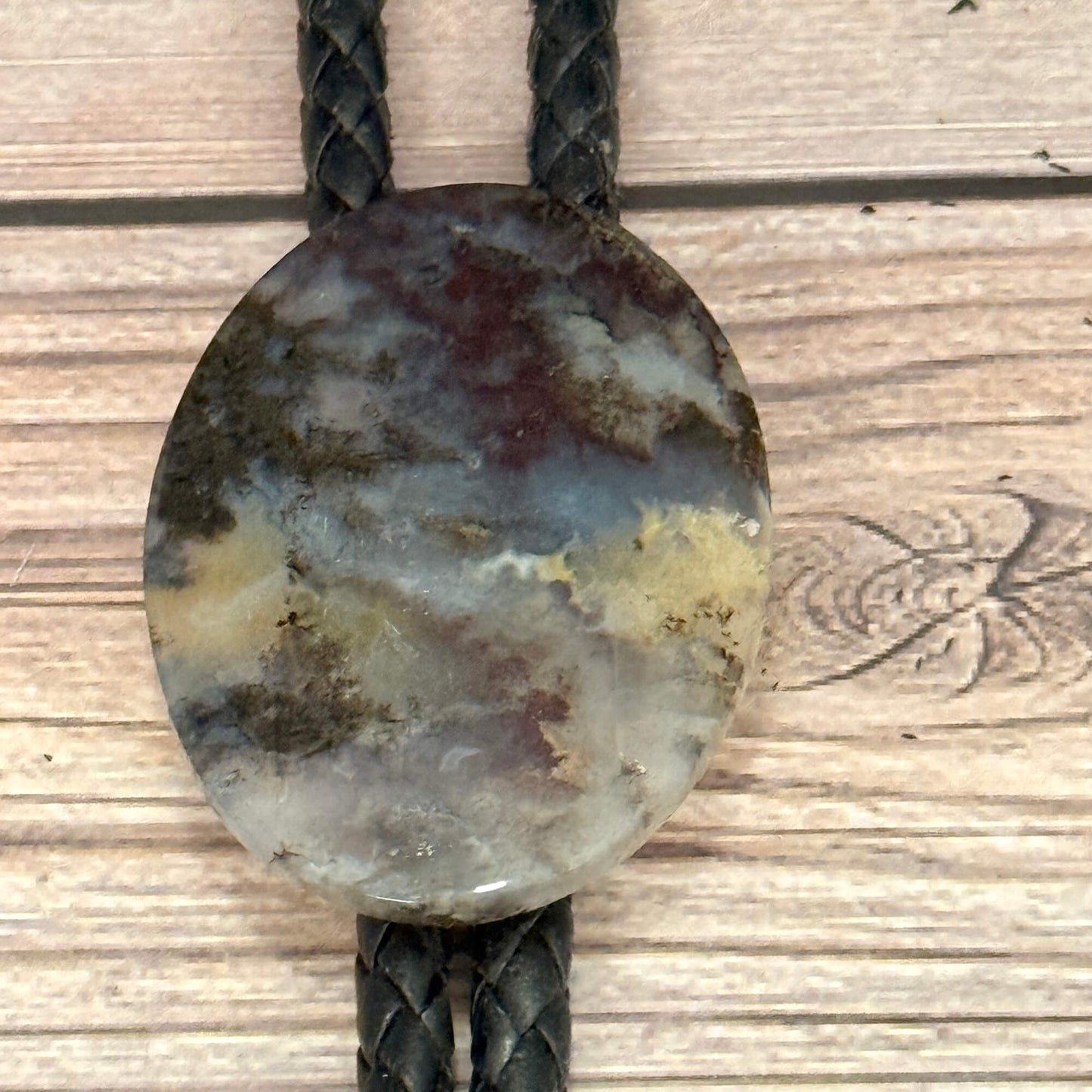 Round stone pendant on a braided leather cord against a wooden background