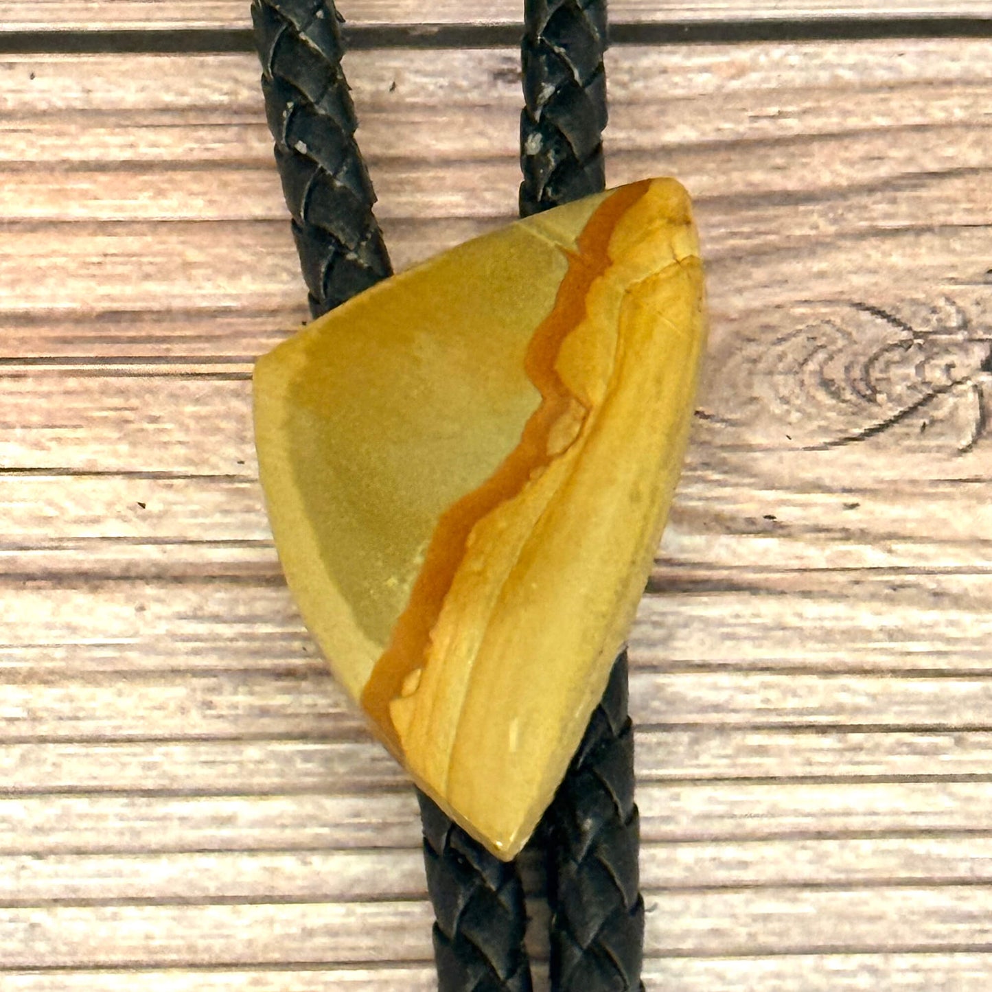 Triangular yellow stone pendant on a braided black cord against a wooden background