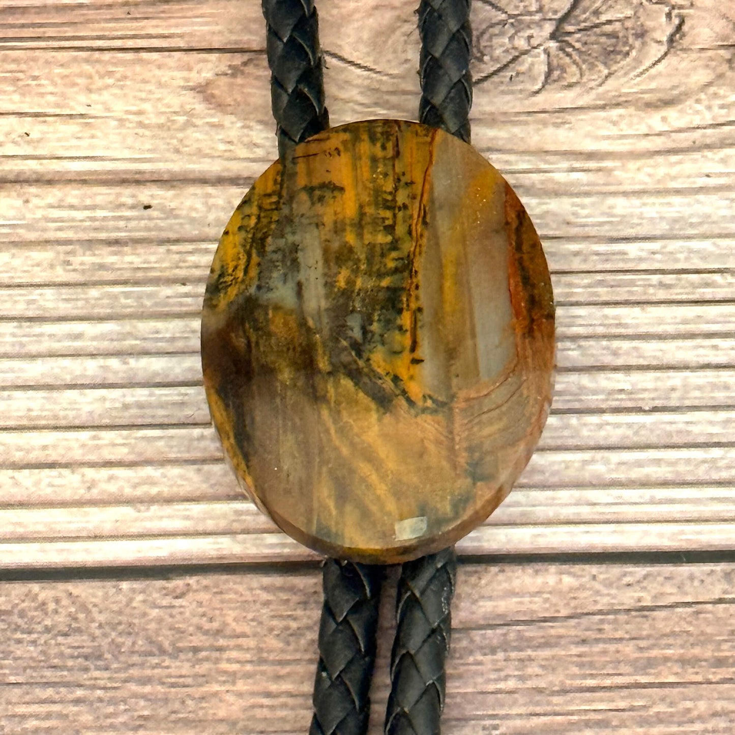 Round petrified wood bolo tie with braided black cord on a wooden surface