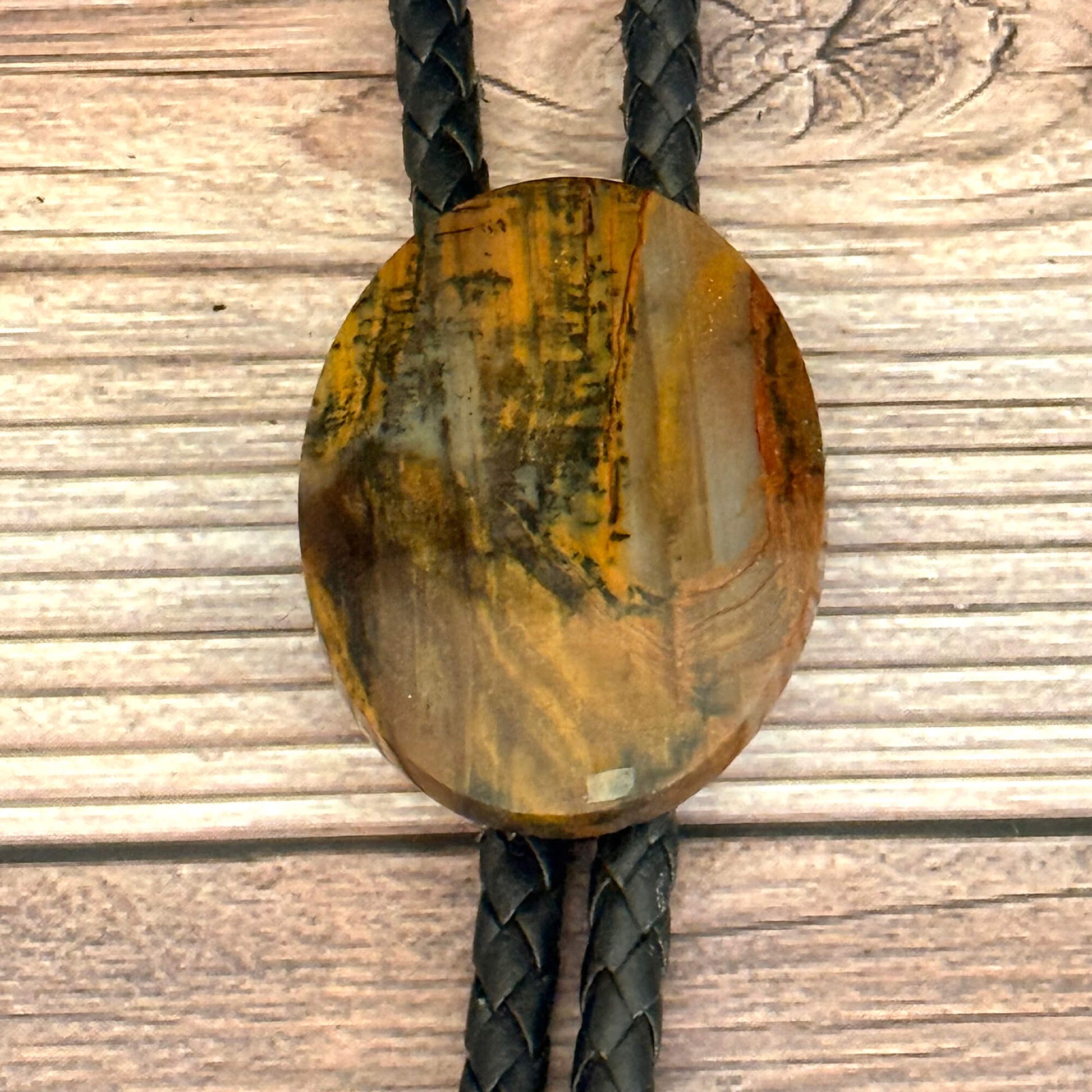 Round petrified wood bolo tie with braided black cord on a wooden surface