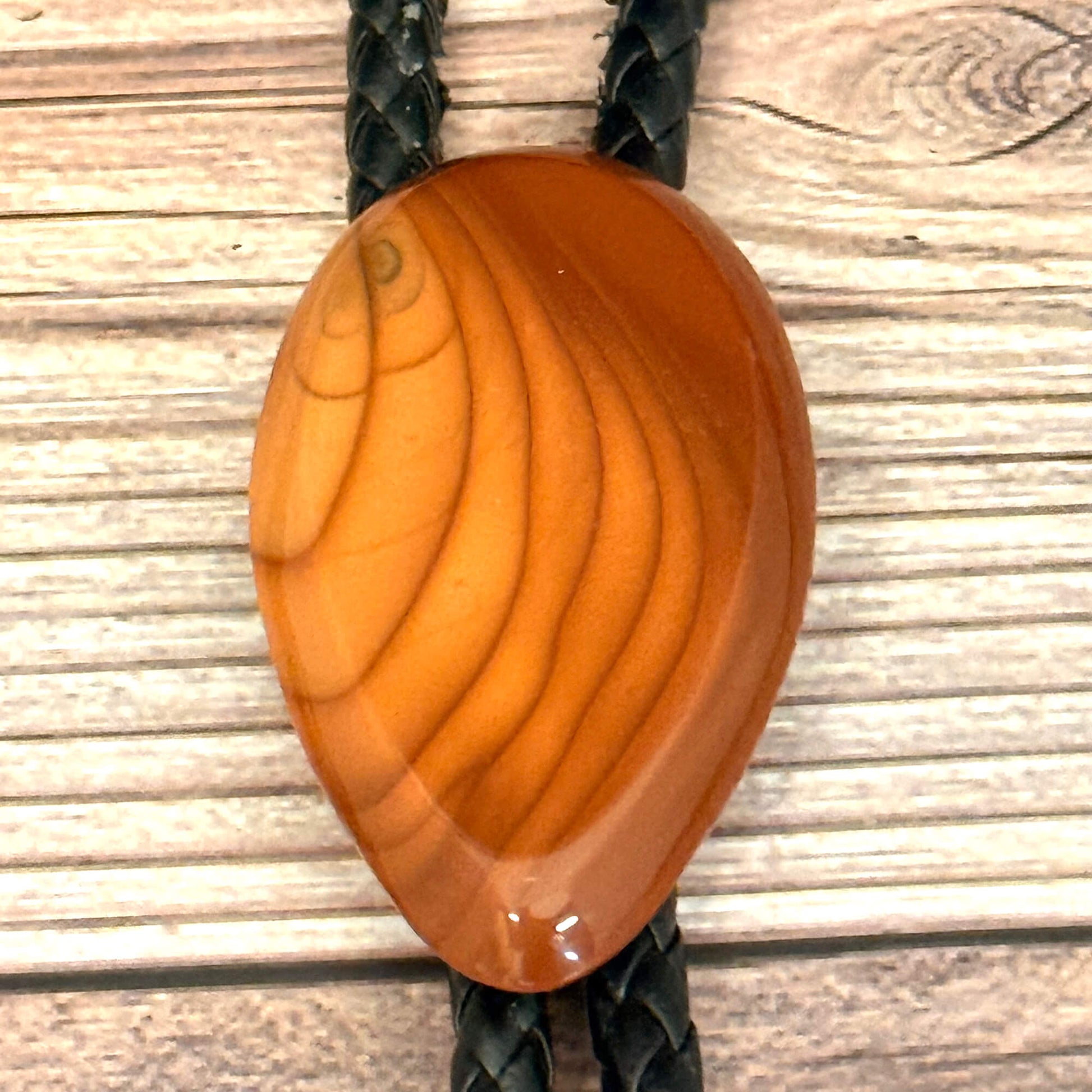 Stone bolo tie with braided design on a wooden surface