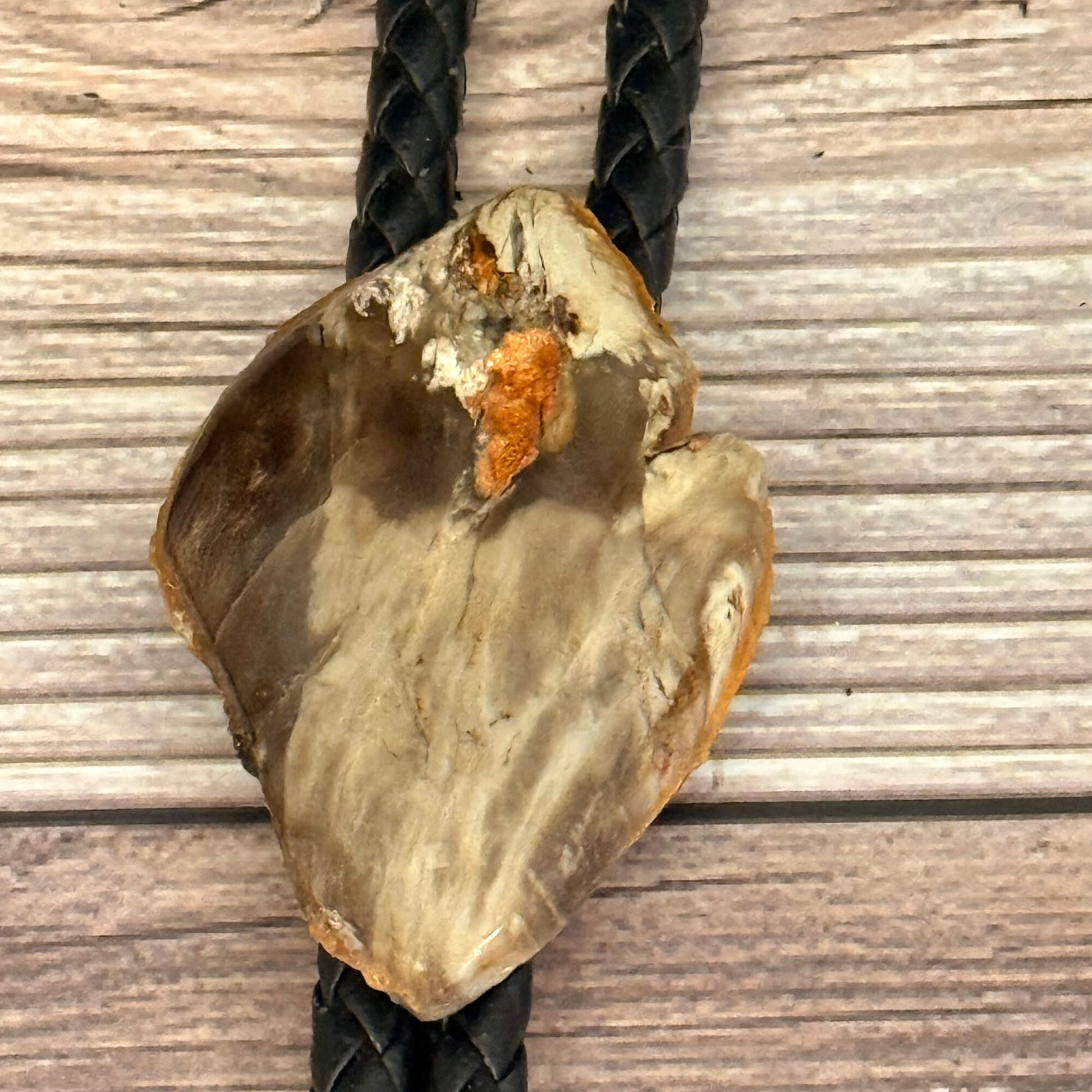 Raw stone pendant on a black cord against a wooden background