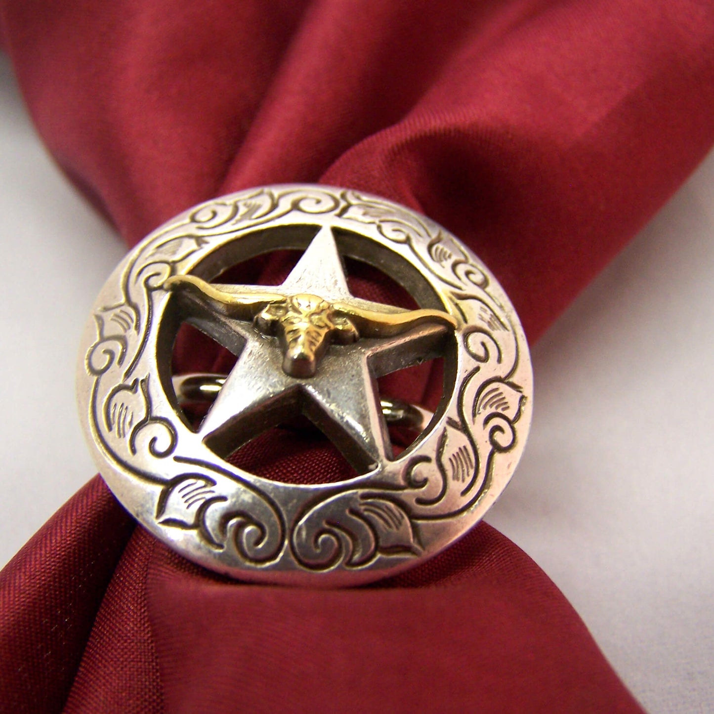 Secure your wild rag with a Cattle Kate Scarf Slide. This design features a brass longhorn centered on a Texas star of solid nickle. An etched design borders the round slide measuring 1 1/2" diameter this slide is sure to last.