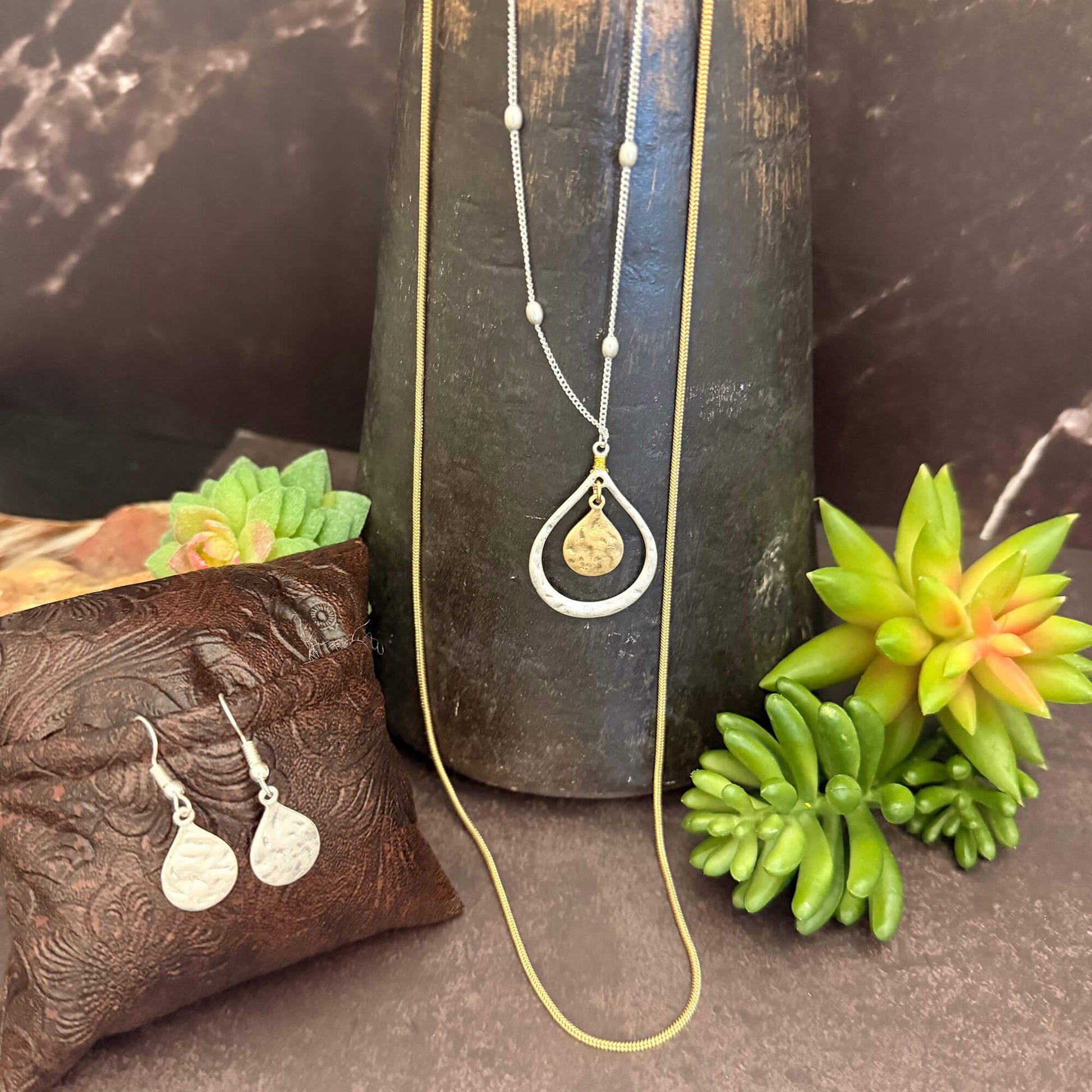 Jewelry set with necklace and earrings on a dark surface with succulents
