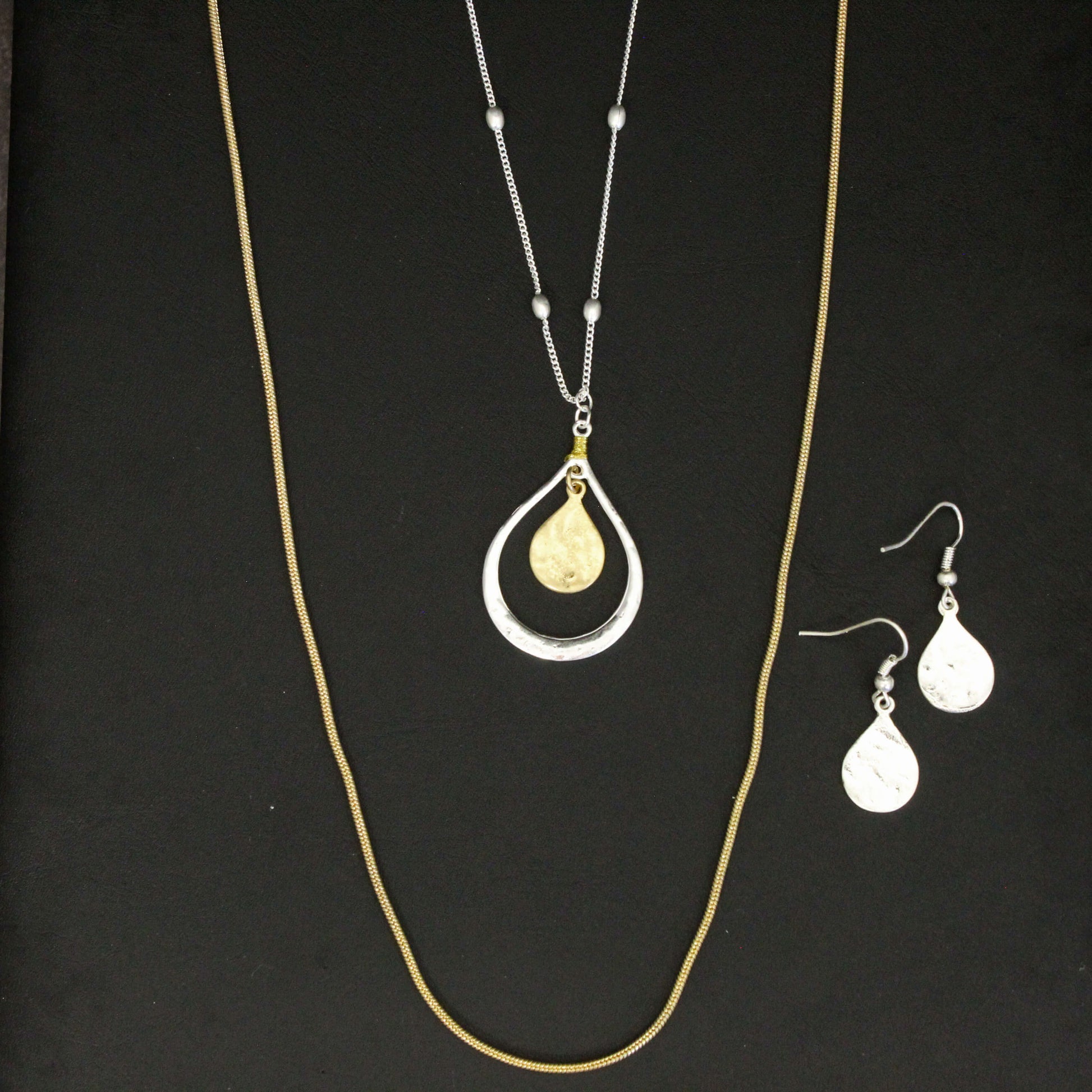 Gold necklace with a teardrop pendant and matching earrings on a black background