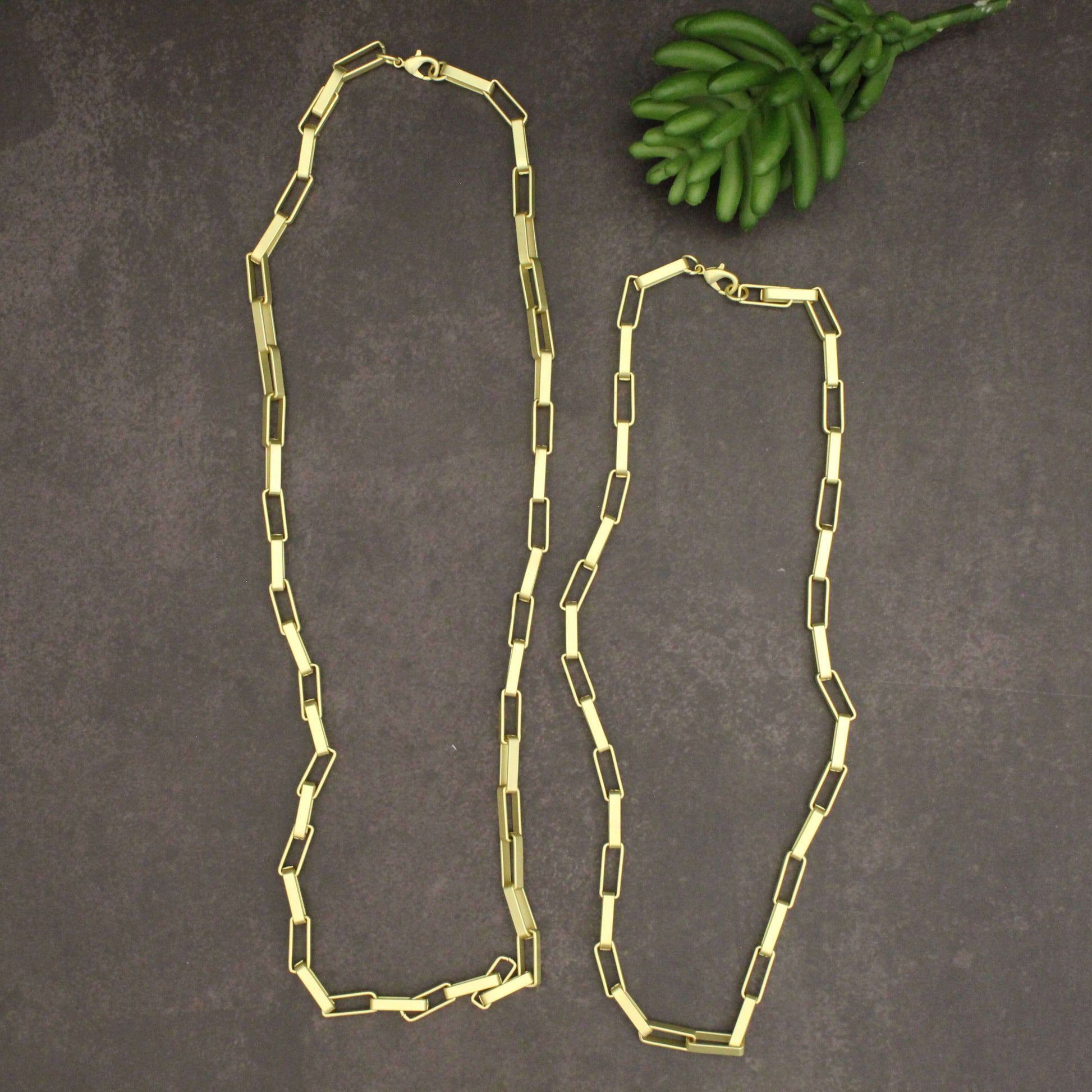 Gold chain necklace on a dark surface with green leaves.