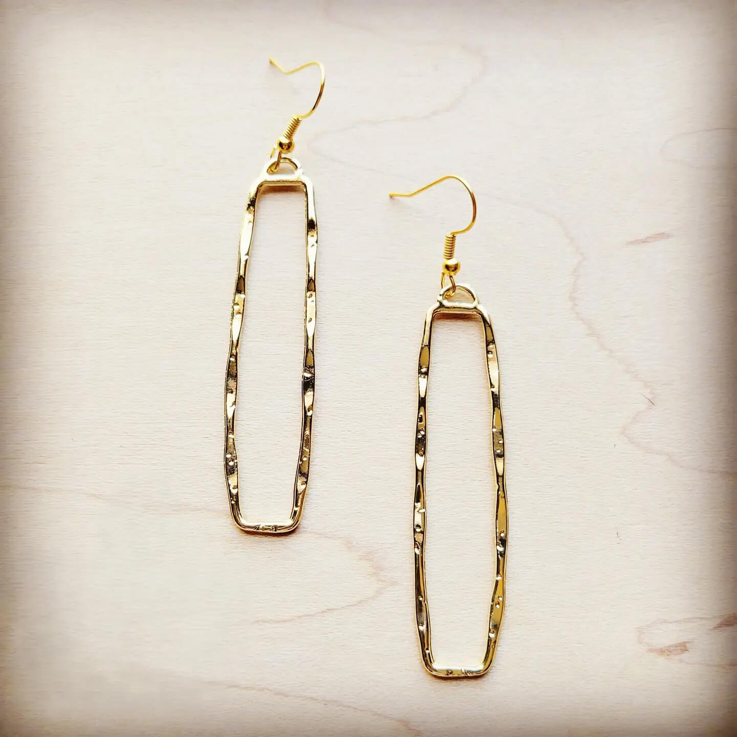 Gold dangle rectangle earrings on a beige marble background