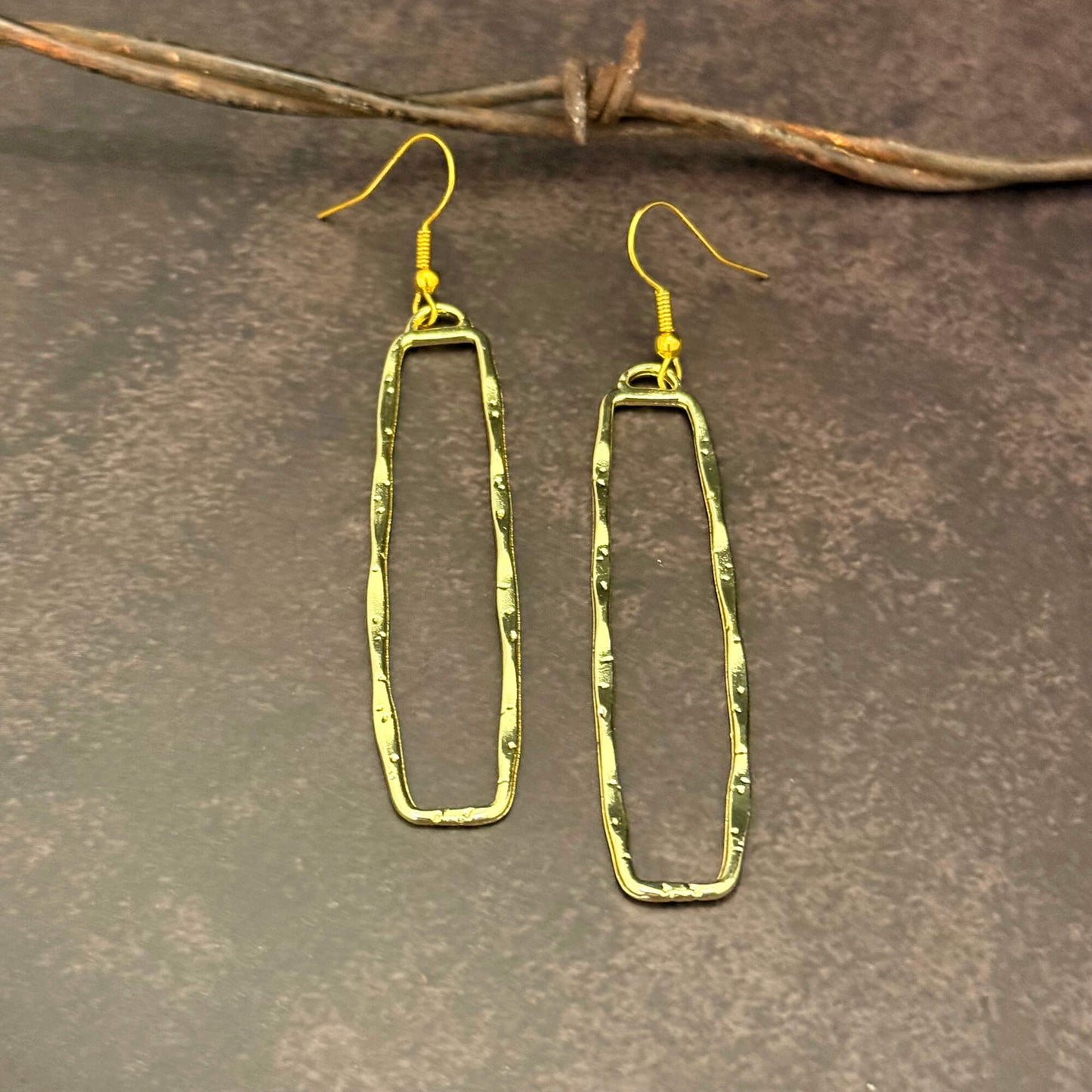 Gold Dangle Rectangle earrings on a textured brown surface