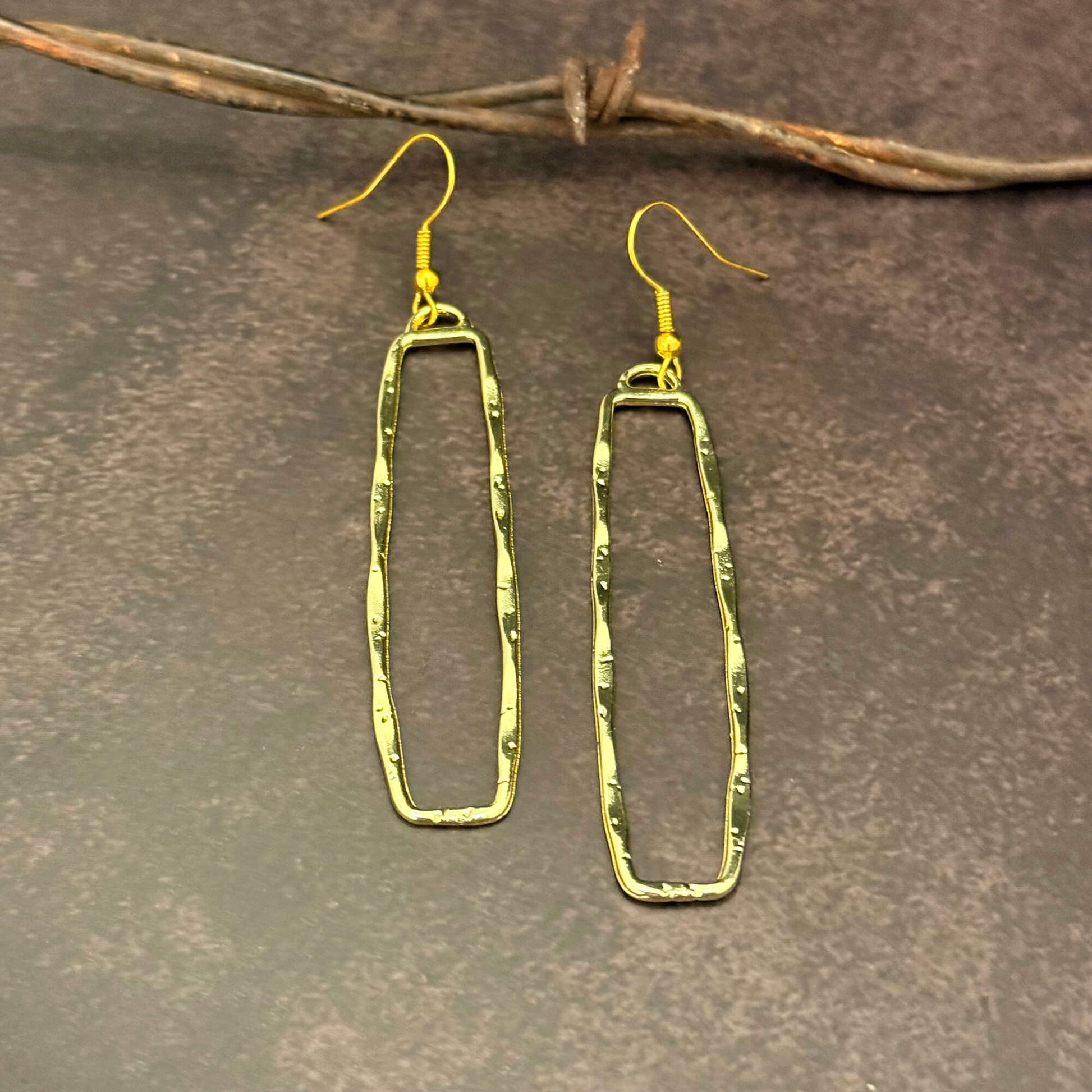 Gold Dangle Rectangle earrings on a textured brown surface