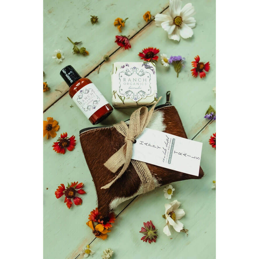 Product set with a bottle, bar of soap, and pouch on a light green background with flowers.