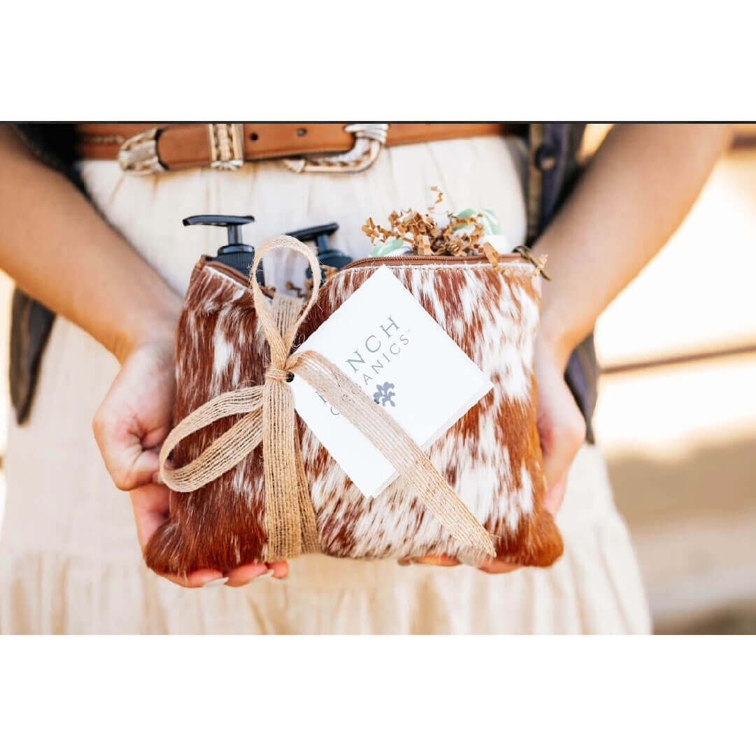 Person holding a cowhide clutch bag with a bow and a card inside, blurred background