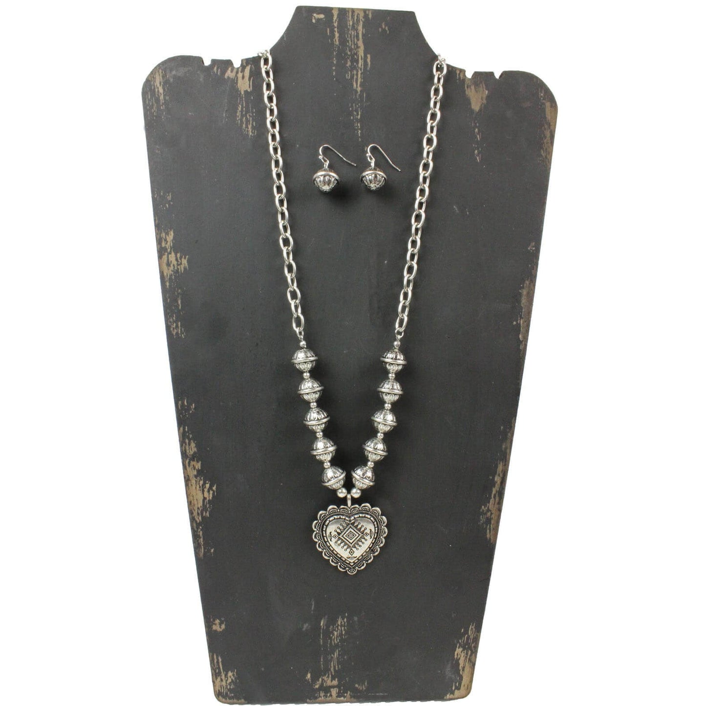 Large silver tone chain links and oversized silver beads lead to an embossed heart pendant. Necklace measures 28″ with lobster claw clasp and extension chain. Matching earrings on hypoallergenic ear wires