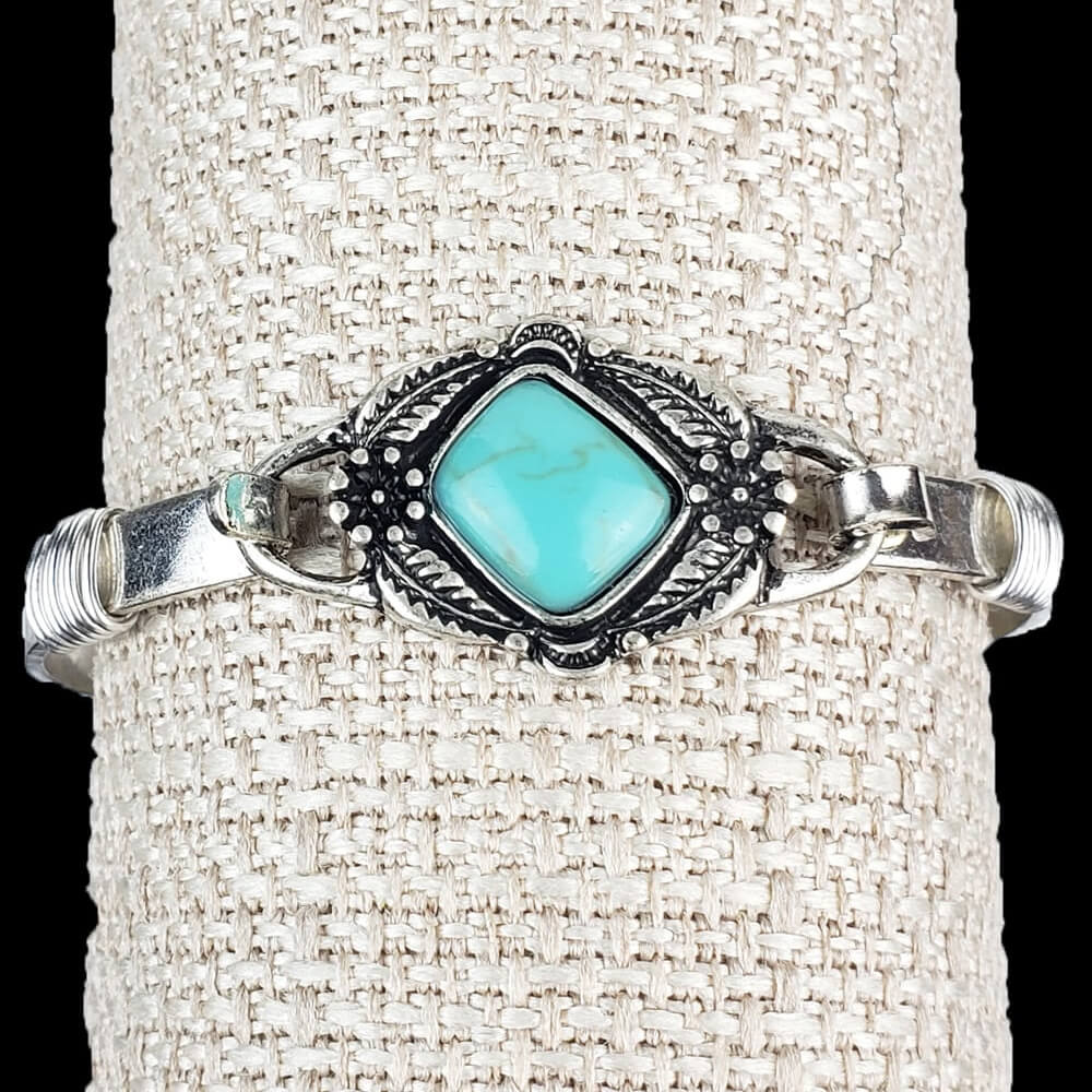 Silver hinged band with a flower framed plate. Adorned with a magnesite turquoise stone. Measures 2.5″ in diameter.