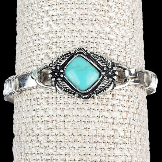 Silver hinged band with a flower framed plate. Adorned with a magnesite turquoise stone. Measures 2.5″ in diameter.