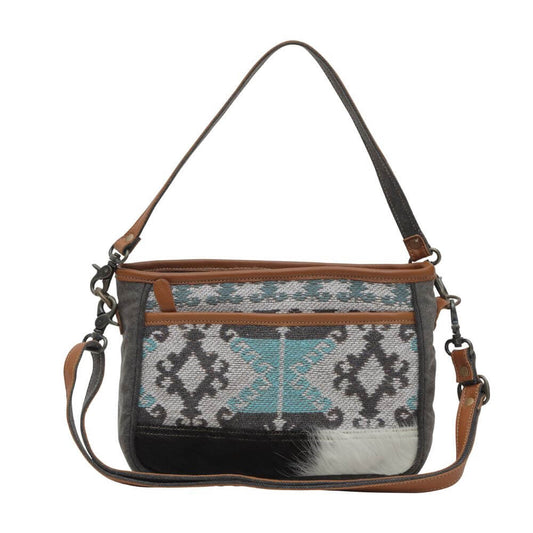 This little charmer brings big cowgirl flair with its canvas prints in dusty blues and weathered greys. Constructed from durable canvas with genuine leather accents, it's built to last through all your adventures. The compact size carries just the essentials while the crossbody strap keeps your hands free. Measures 11" by 8"