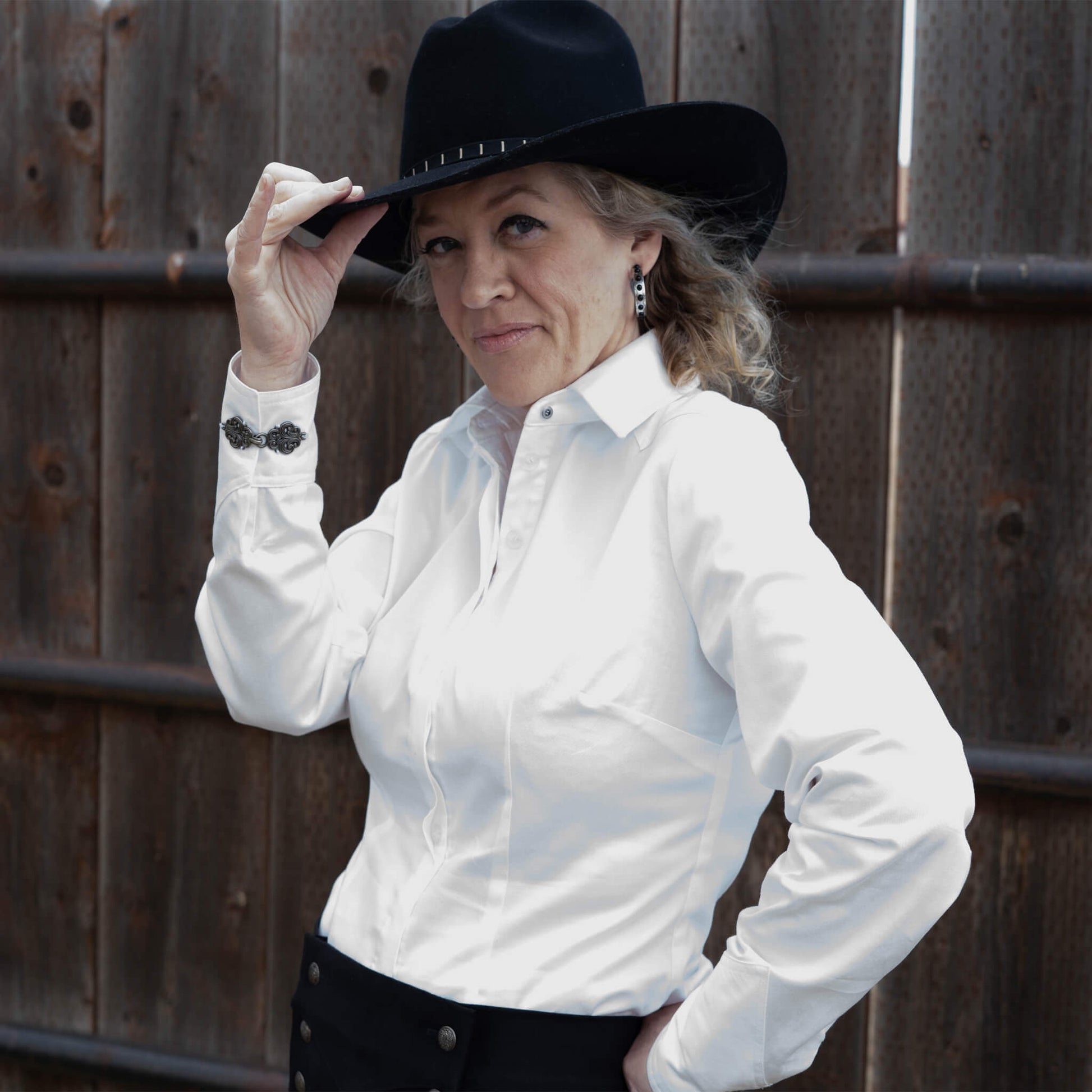 Go from riding your horse, to the office and then a night out on the town in this classy and versatile blouse. Great for any event! Designed with fitted darts in front and back, a hidden button placket and angular cuffs charmed with silver Ingrid clasps. Now designed with front and back yoke for more western flair! Order in white or black 100% cotton sateen. Made in USA.