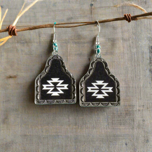 Stunning ladies western cow tag southwest earrings featuring a unique dangle design, on a striking matte black cow tag shape adorned with an elegant white Southwest pattern. Perfect for both casual and formal occasions, these earrings are a must-have for those who appreciate distinctive Western-inspired jewelry. French Hook Style. Measure 2" long by 1-1/4" wide.