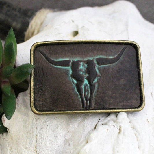 A stunning western accessory featuring a striking longhorn skull design in rich brown and turquoise hues, this buckle adds a touch of rustic charm to any outfit. Perfect for ladies who appreciate unique western flair, this super cute buckle is not just a fashion statement but also a durable piece that will stand the test of time. Measures 3x2 inches and is proudly crafted in the USA.
