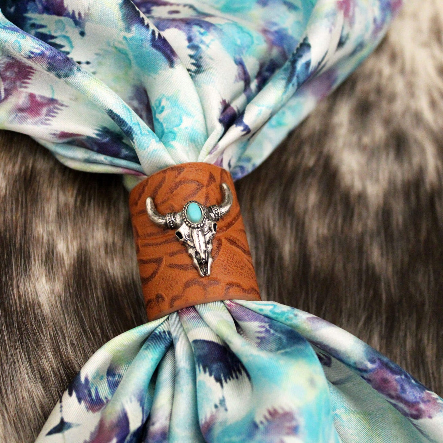 Saddle up your style with the one-of-a-kind Leather Longhorn Slide. Crafted from rich embossed brown leather and studded with a silver skull and dazzling turquoise stone, this 1-1/2" x 1" diameter slide adds western flair to any scarf or rag.