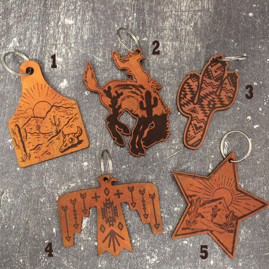 This leather keychain lassos your keys with western charm. The painted leather depicts scenes of horses, cacti, cowboys, and desert landscapes for a touch of the wild west wherever you roam. Stylish and practical, this keychain wrangler keeps your keys from wandering off while showing your western spirit.