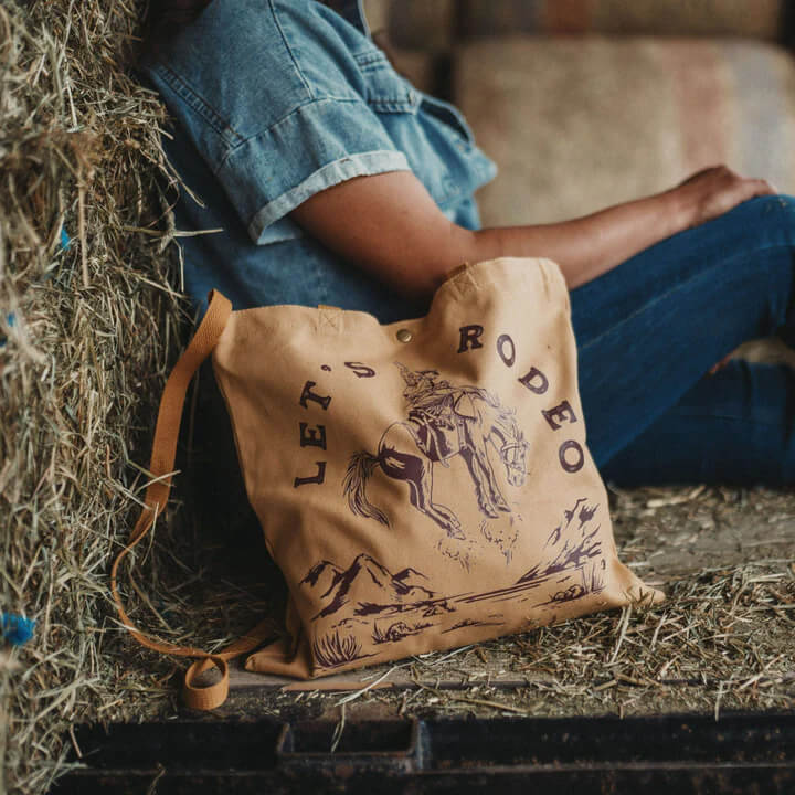 Rodeo design now on a tote! Cotton canvas tote with long shoulder strap, and hand straps. Snap closure at top, and a zip pocket inside, perfect to store your small items! 14"x14" Handwash only! Designed in Montana