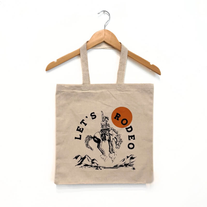 Tote bag with 'Let's Rodeo' design on a hanger against a white background