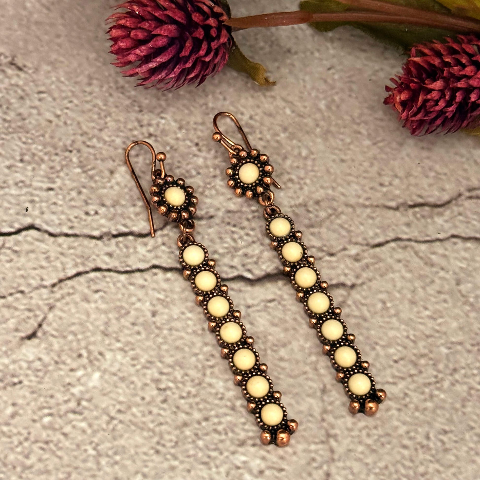 Pair of long earrings with circular beads on a textured surface with pink flowers.