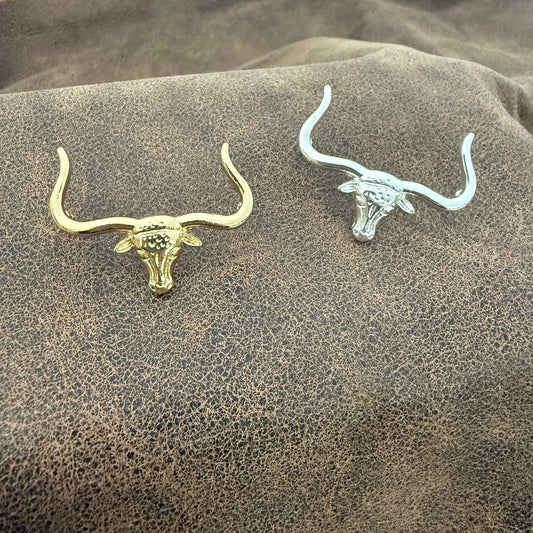 Gold and silver bull skull earrings on a textured brown surface