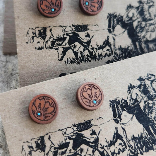 Pair of round leather earrings with embedded stones on a card with horse illustrations.