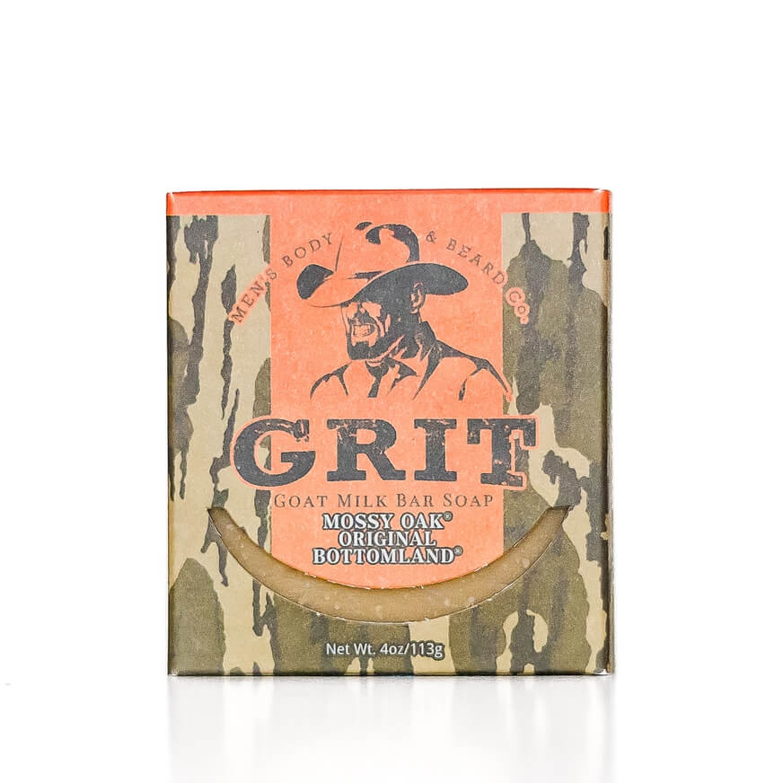 A boxed bar soap product on a white background. The package has a camouflage-style pattern with a large peach panel featuring a cowboy illustration and the prominent text 'GRIT.
