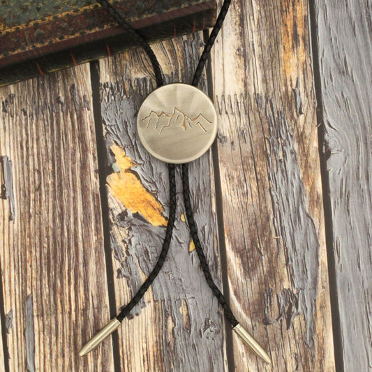 Channel your inner cowboy or rugged outdoorsman with this handsome bolo tie. The etched mountain range design is a bold, eye-catching statement, while the silver bullet tips add a touch of frontier charm. Whether you're dressing up for a special occasion or adding some Western flair to your everyday look, this bolo tie is the perfect accessory to showcase your American pride and adventurous spirit. Made in the USA. Standard 36" length.