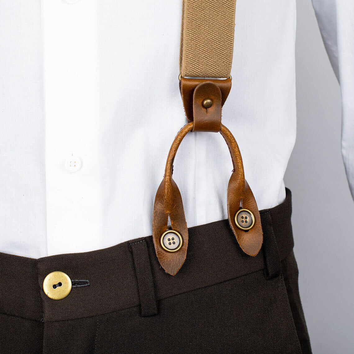 Brown suspenders with leather straps on a white shirt and dark pants.