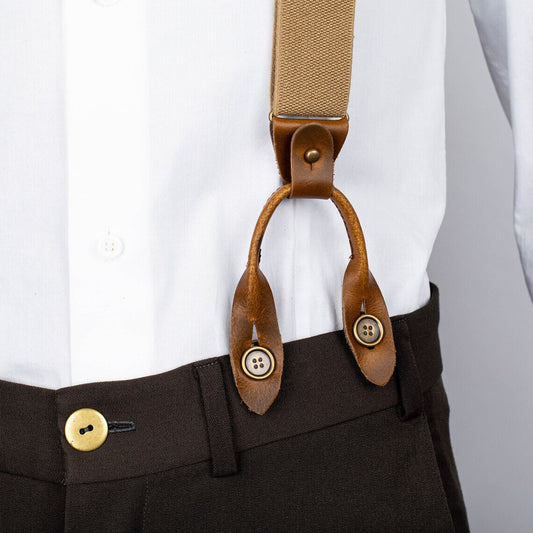 Brown suspenders with leather straps on a white shirt and dark pants.