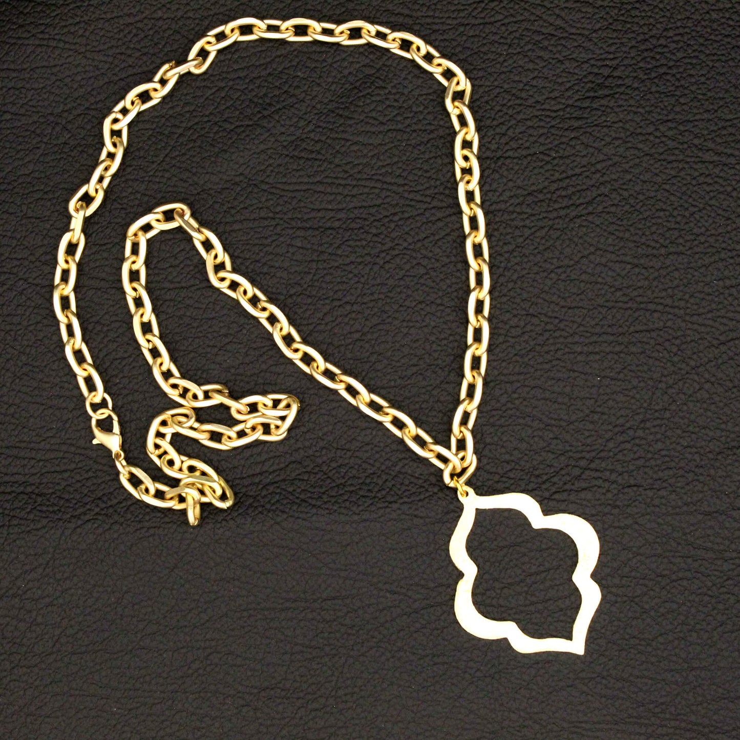 A gold chain necklace with a white cloud-shaped pendant, displayed on a textured black background.