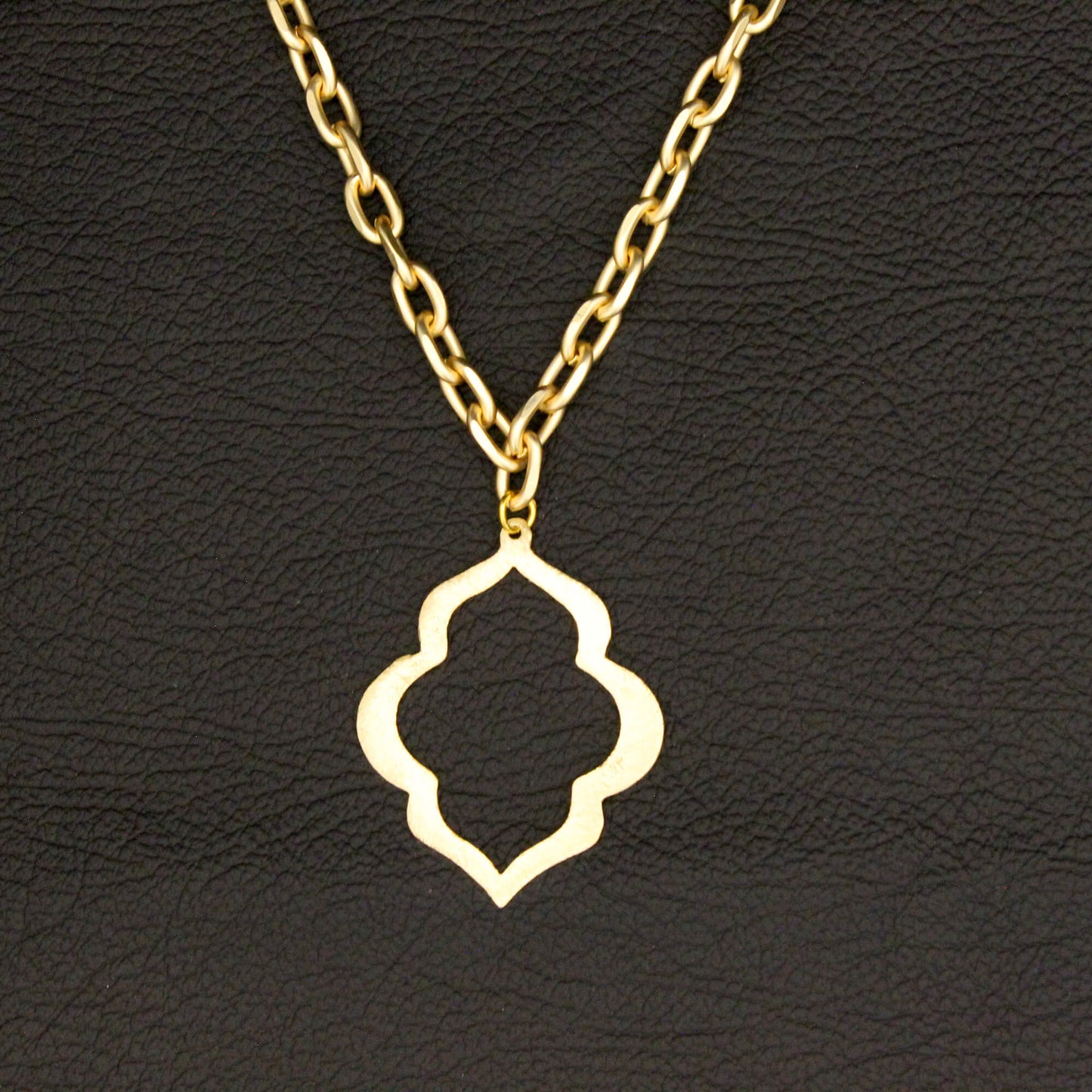 A gold-tone necklace with a four-lobed openwork pendant, displayed against a textured black background.