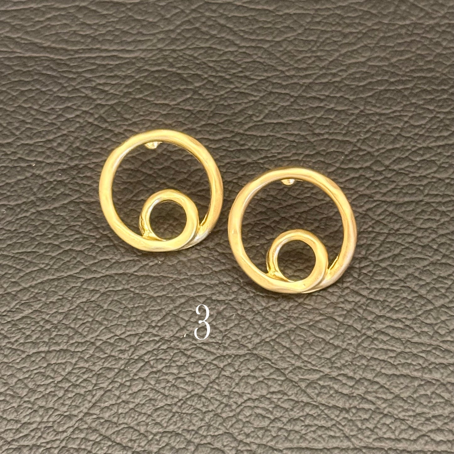 A pair of gold-toned spiral hoop earrings displayed on a textured dark gray surface.