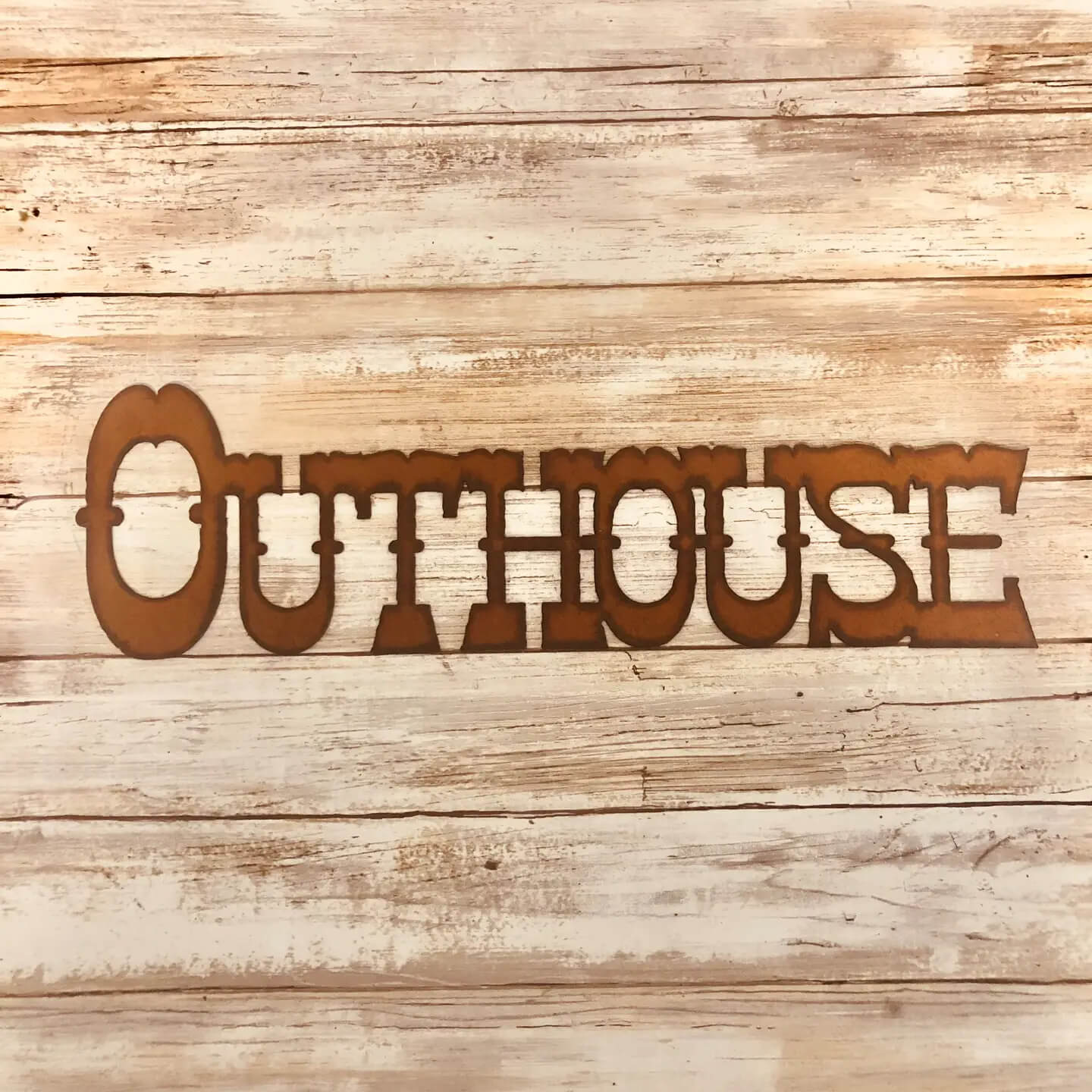 A laser-cut metal wall sign spelling 'OUTHOUSE' in a rustic brown color, displayed against a light-colored, weathered wood plank background.