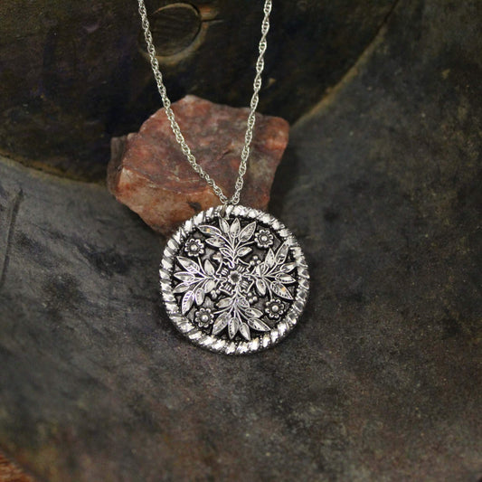 Pewter embossed circle pendant with a floral and leaf pattern in Victorian style. Timeless piece of jewelry. Celebrate your unique style with our classic western jewelry. Each piece is handmade and hand finished with diamond cuts. The sparkly cuts give each piece a unique dazzling sparkle. Approximately 1-1/2" diameter. Made in USA