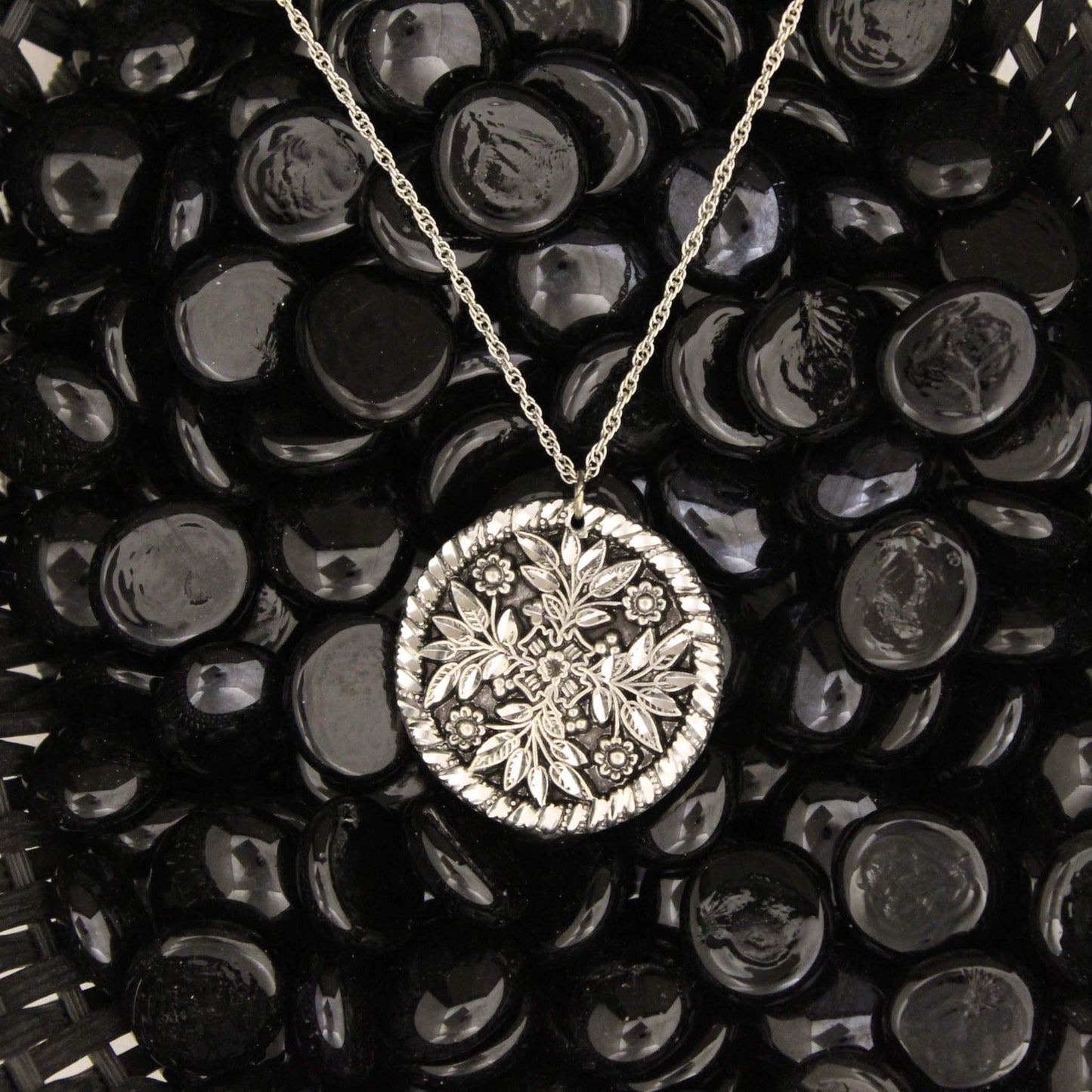 Pewter embossed circle pendant with a floral and leaf pattern in Victorian style. Timeless piece of jewelry. Celebrate your unique style with our classic western jewelry. Each piece is handmade and hand finished with diamond cuts. The sparkly cuts give each piece a unique dazzling sparkle. Approximately 1-1/2" diameter. Made in USA