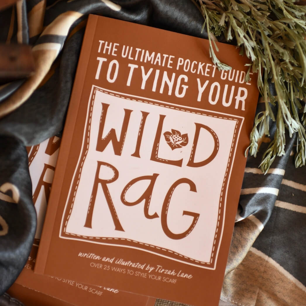 Book titled 'The Ultimate Pocket Guide to Tying Your Wild Rag' on a textured fabric background