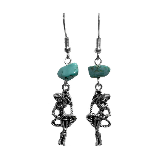 A pair of silver-toned dangle earrings featuring a small turquoise-colored stone and a dangling cowgirl figure charm, shown against a plain white background.
