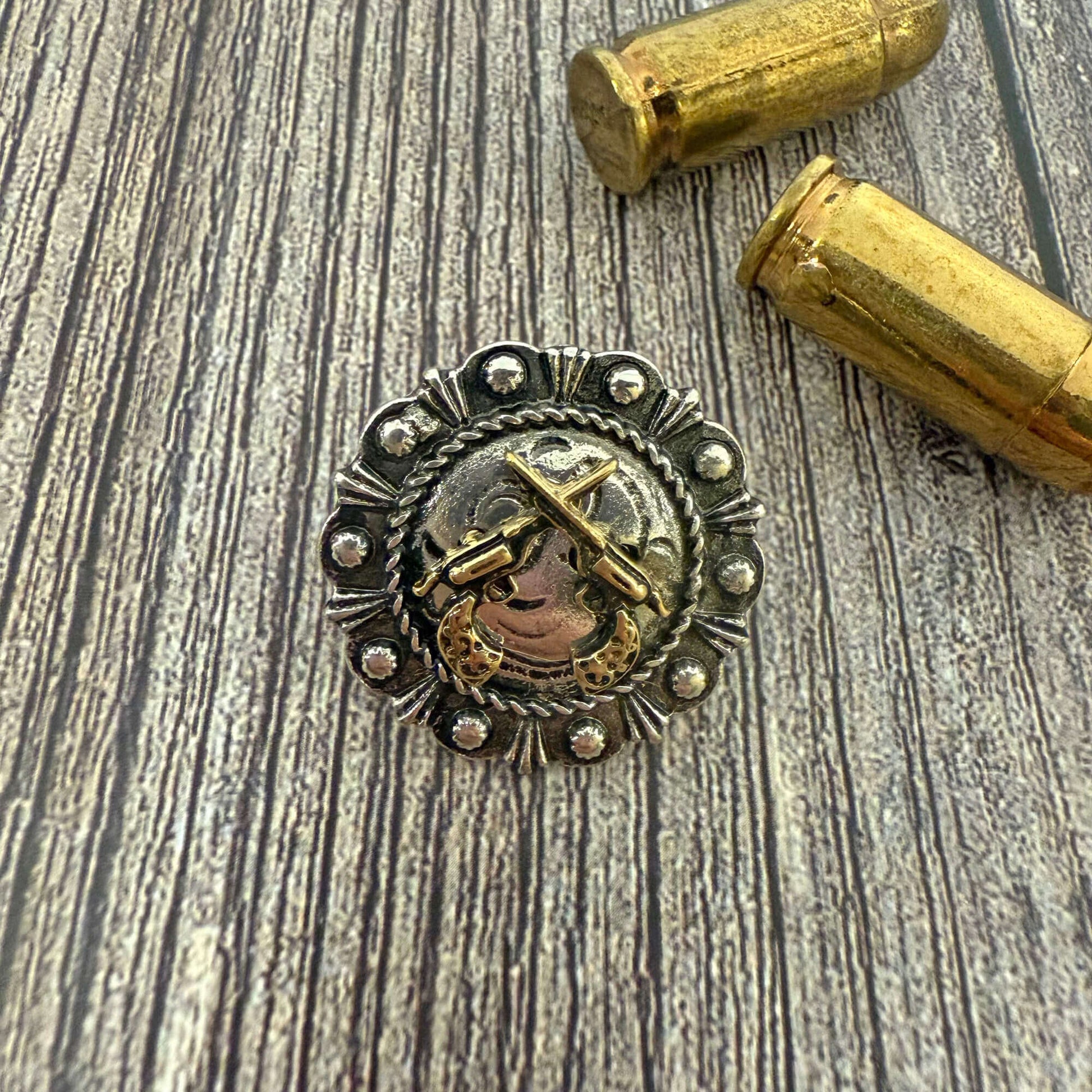 Decorative metal button with intricate design on a wooden surface with two gold bullets.