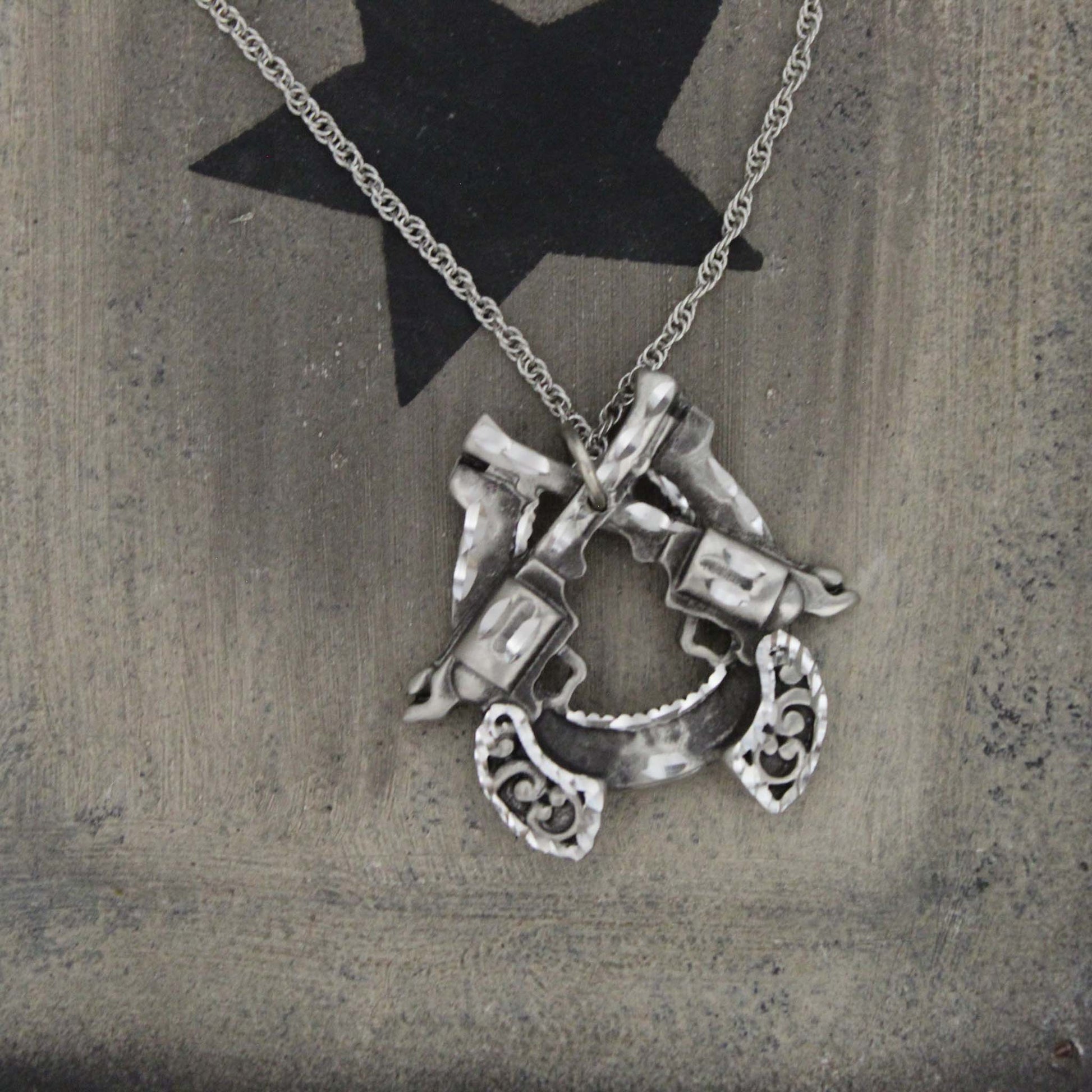 Show off your the bold cowgirl in yourself with this unique pewter necklace in the shape of a horseshoe with two pistols on an 18" chain. Each piece is handmade and hand finished with diamond cuts. The sparkly cuts give each piece a unique dazzling sparkle. Approximately 1-1/2" wide by 1-1/2" long. Made in USA